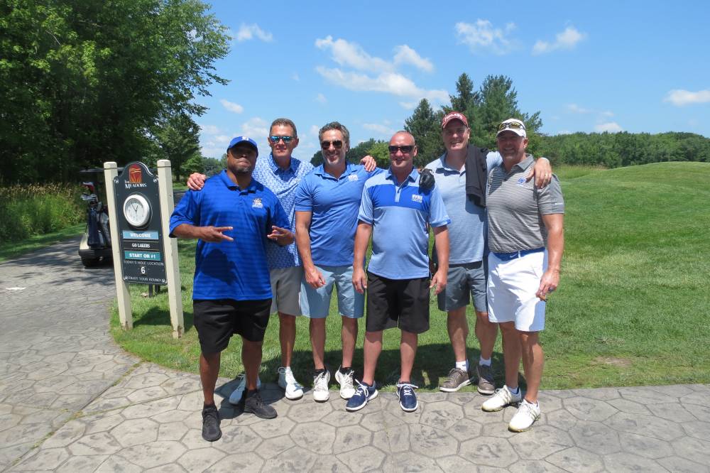 Six football alums standing in front of the golf course.